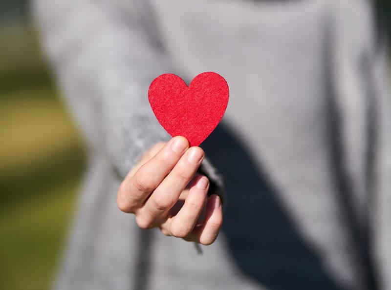 hand som håller fram rött hjärta.